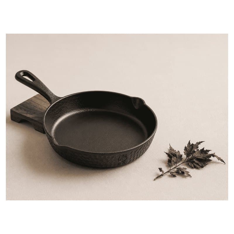 A black cast iron nambu tekki skillet on a beige background with purple leaves.